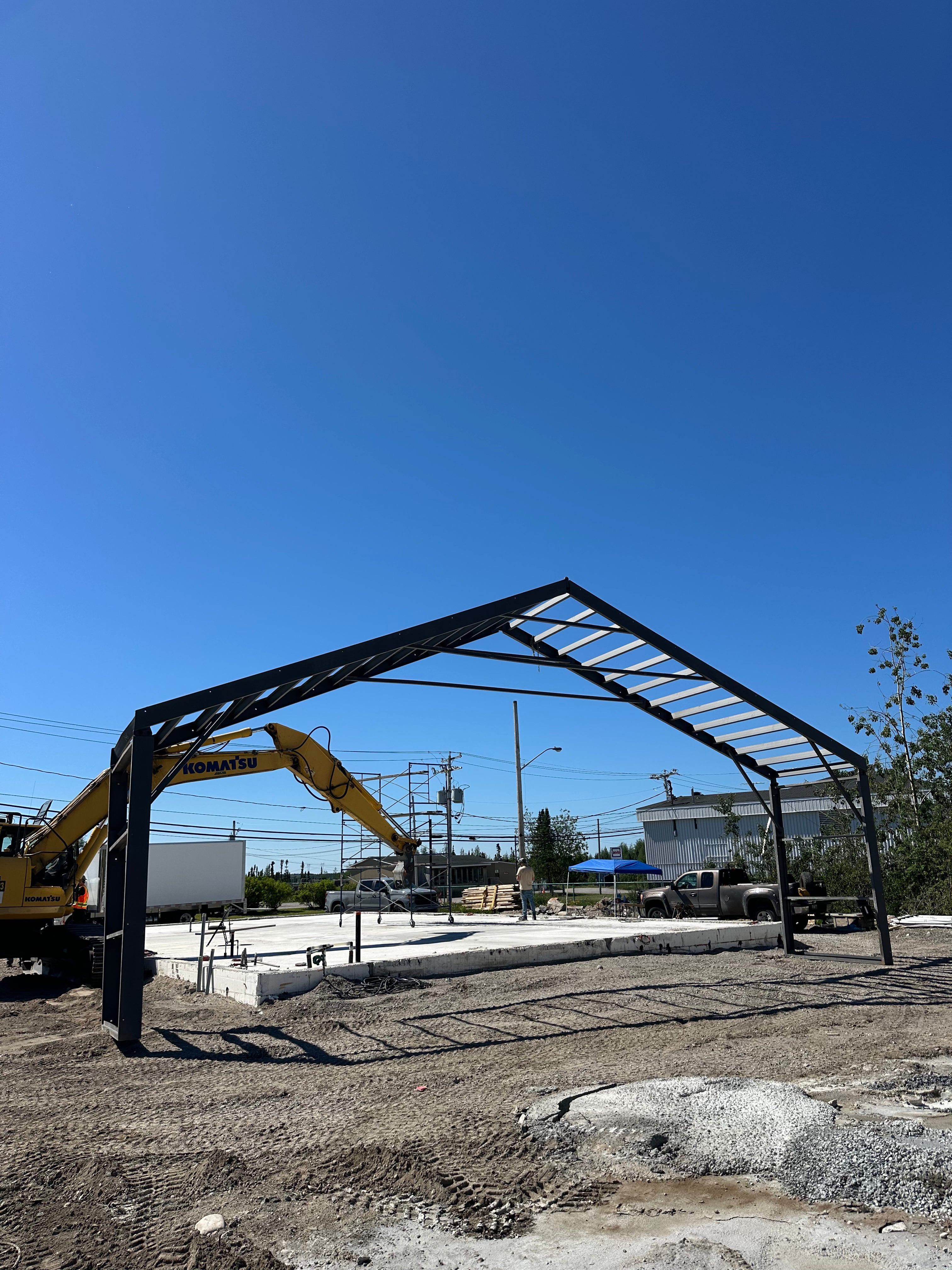 Construction site with a large metal frame and excavator under a clear blue sky.