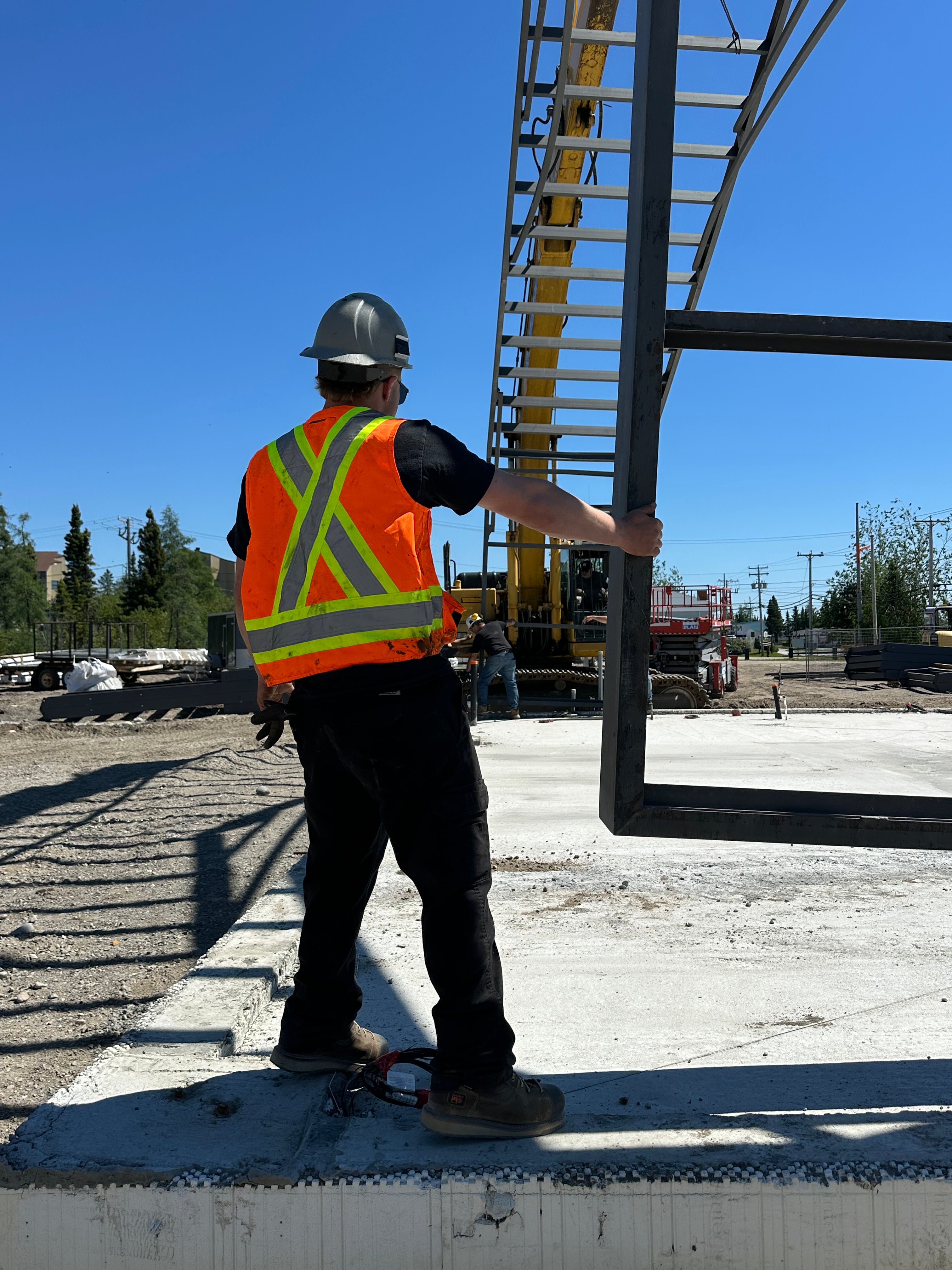 Young construction man holding a metal structure with one hand with a machine in the background