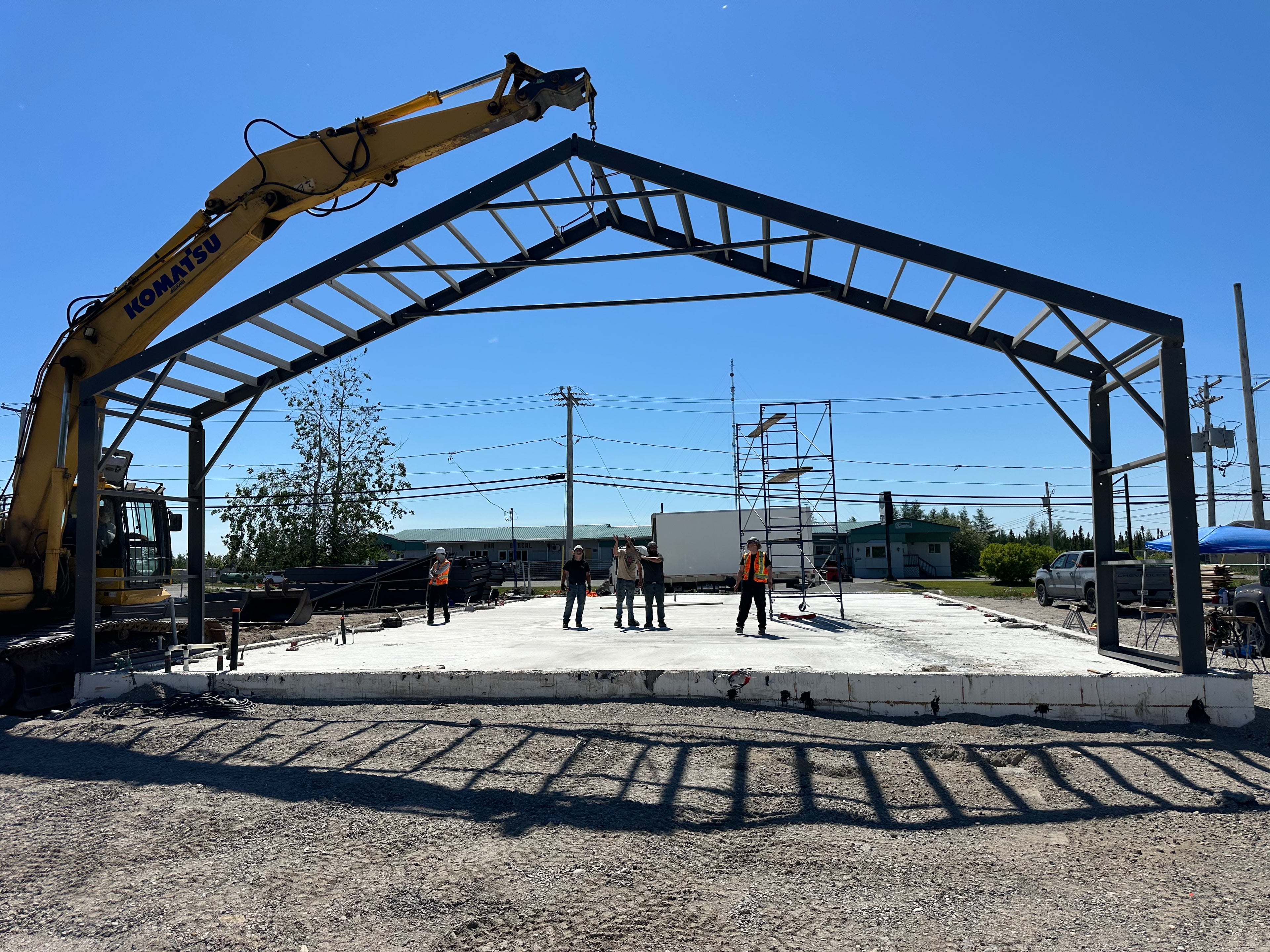 Construction site with a large metal frame structure being assembled under a clear blue sky.