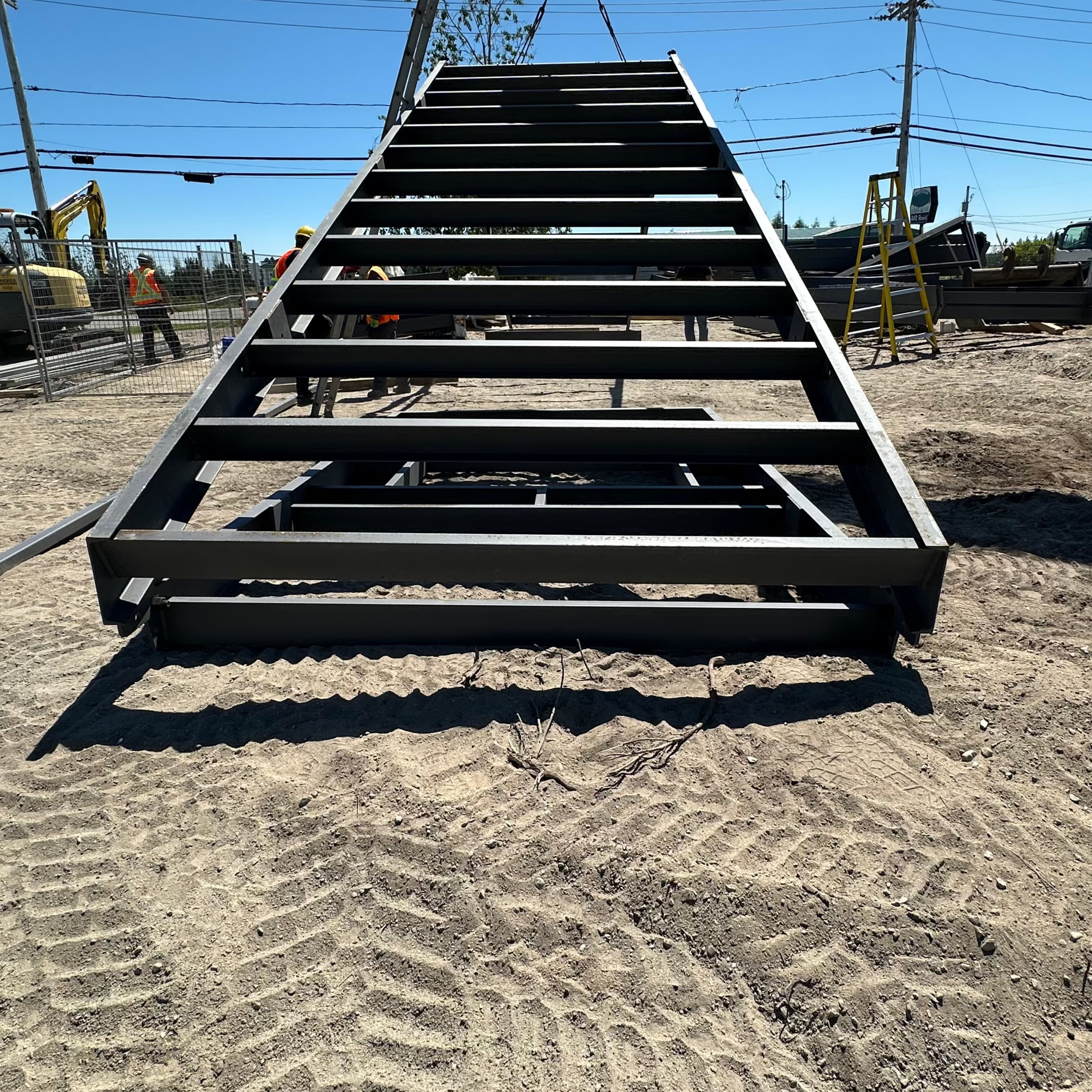 Large metal staircase on a dirt ground with workers and equipment in the background.