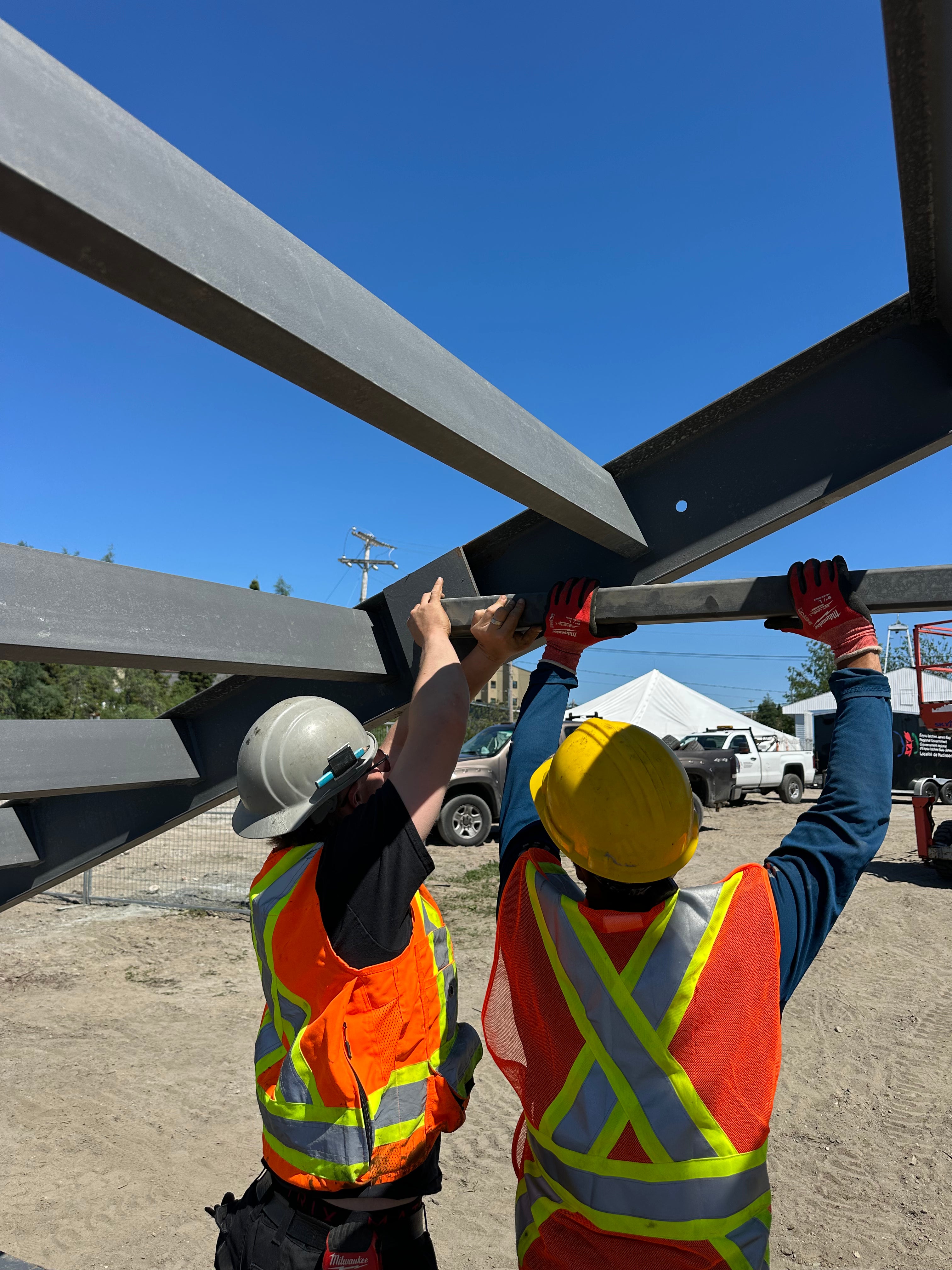 Two construction workers lifting a metal beam outdoors on a clear day.